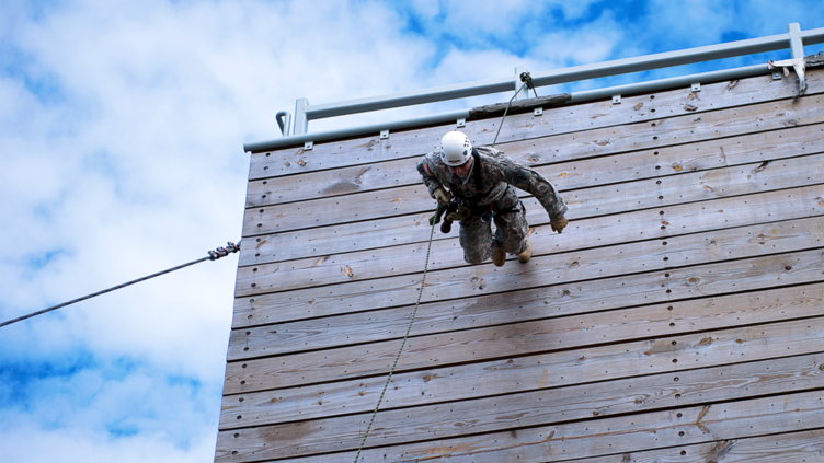 Soldier rappelling down a wooden wall on a training course