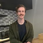 Man smiling the camera while leaning on a counter