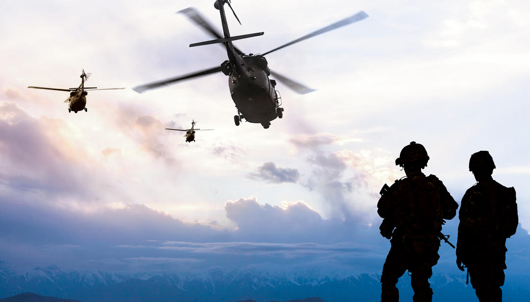 silhouette of two soldiers with helicopters in the sky