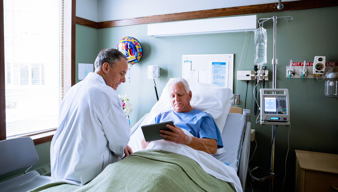 Man in hospital bed with doctor review information on tablet