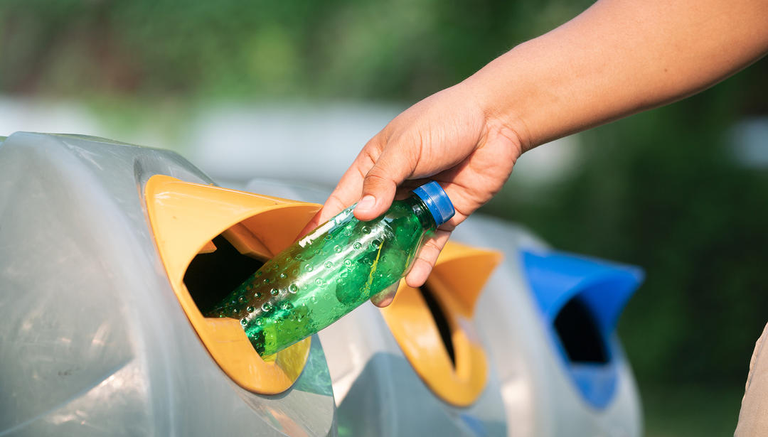 Person placing a plastic bottle into a recycling bin