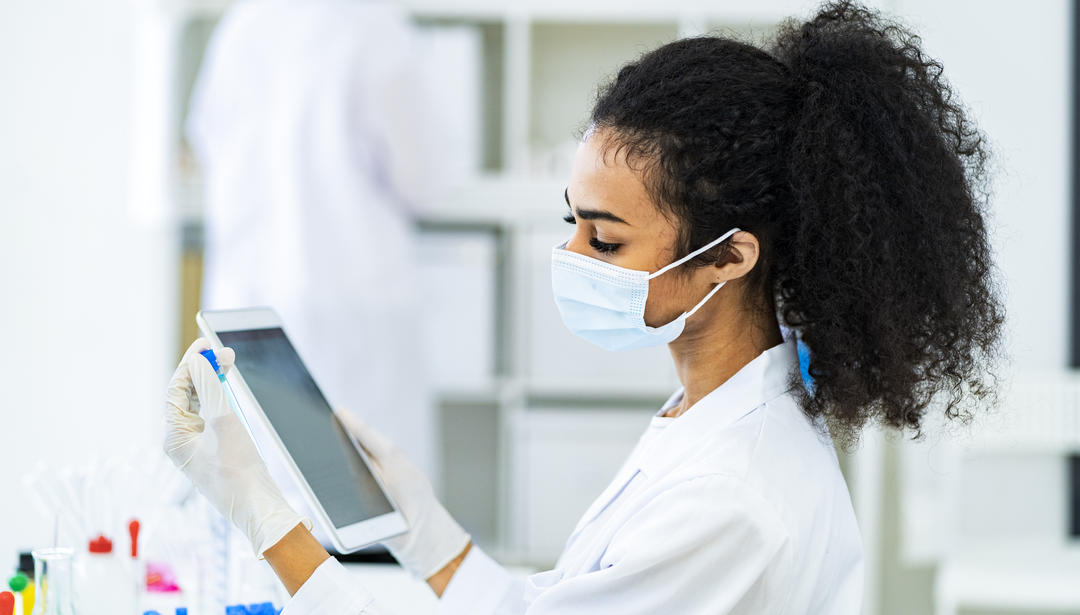 A masked female technician working on an ipad