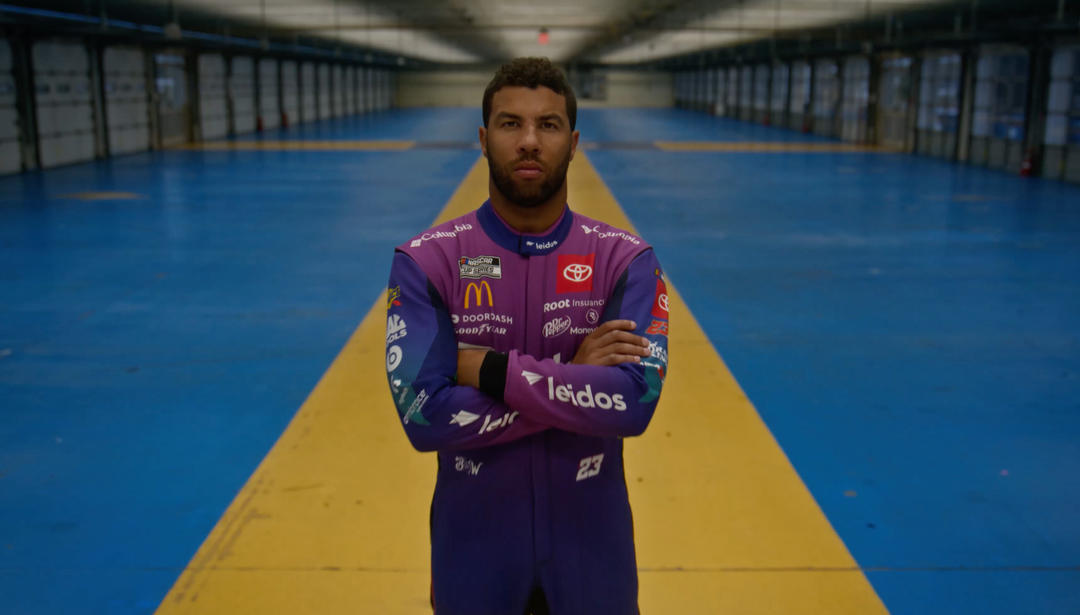 NASCAR driver Bubba Wallace standing with arms crossed in an empty garage