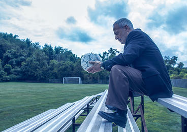 man sitting on bleachers holding soccer ball