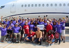 Leidos employees and volunteers from Special Olympics Virginia pose in front of an airplane at the 2022 Dulles Day Plan Pull. 
