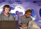 Two men in an airplane wearing headsets working on computers