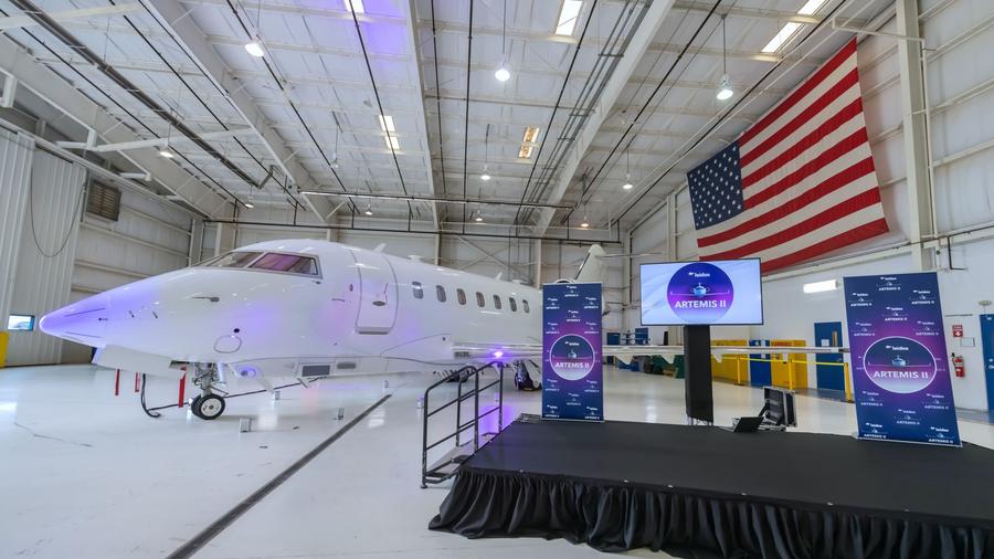 The ARTEMIS II aircraft parked in a hanger with the American flag draped in the background
