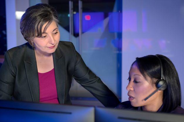 A woman looking at another woman with a headset at a computer
