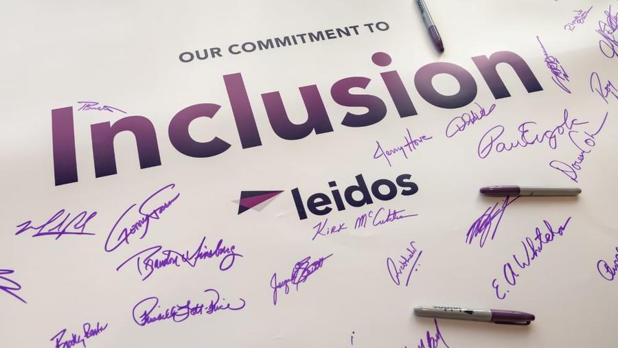 A poster featuring the word "inclusion" signed by several Leidos employees