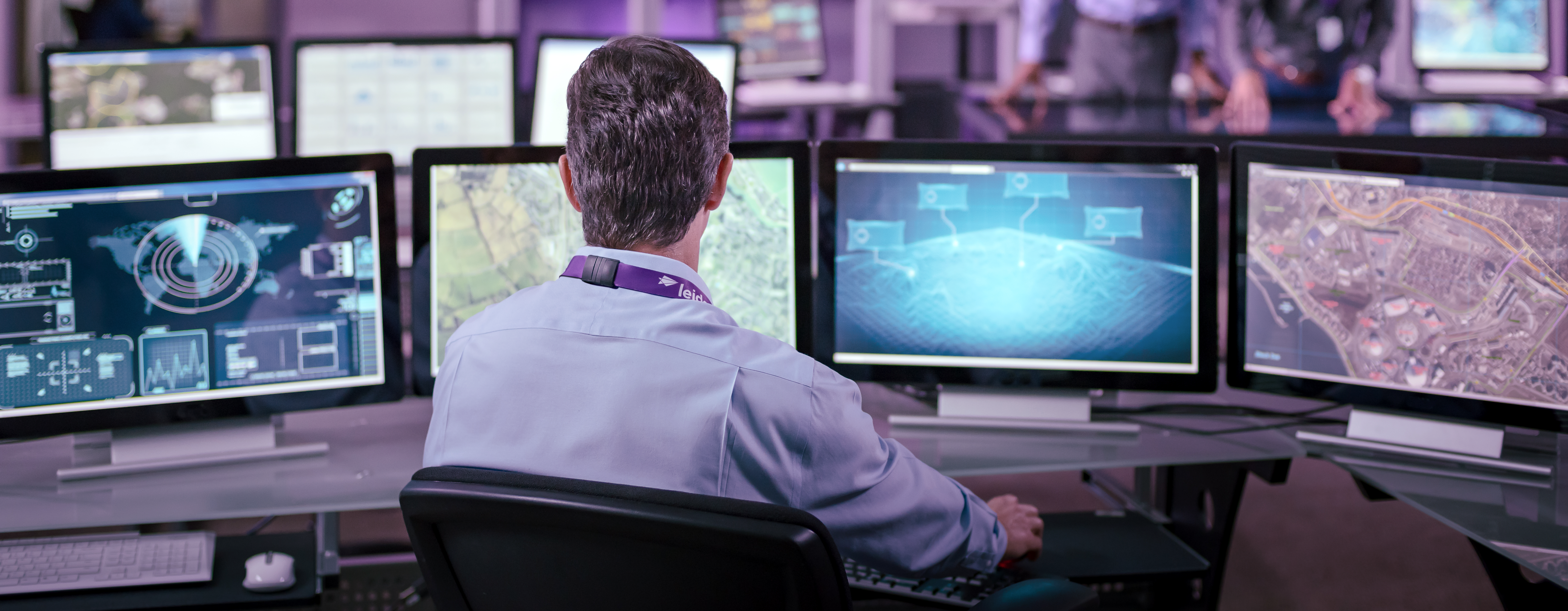 A man with a Leidos lanyard sitting in front of four computer screens