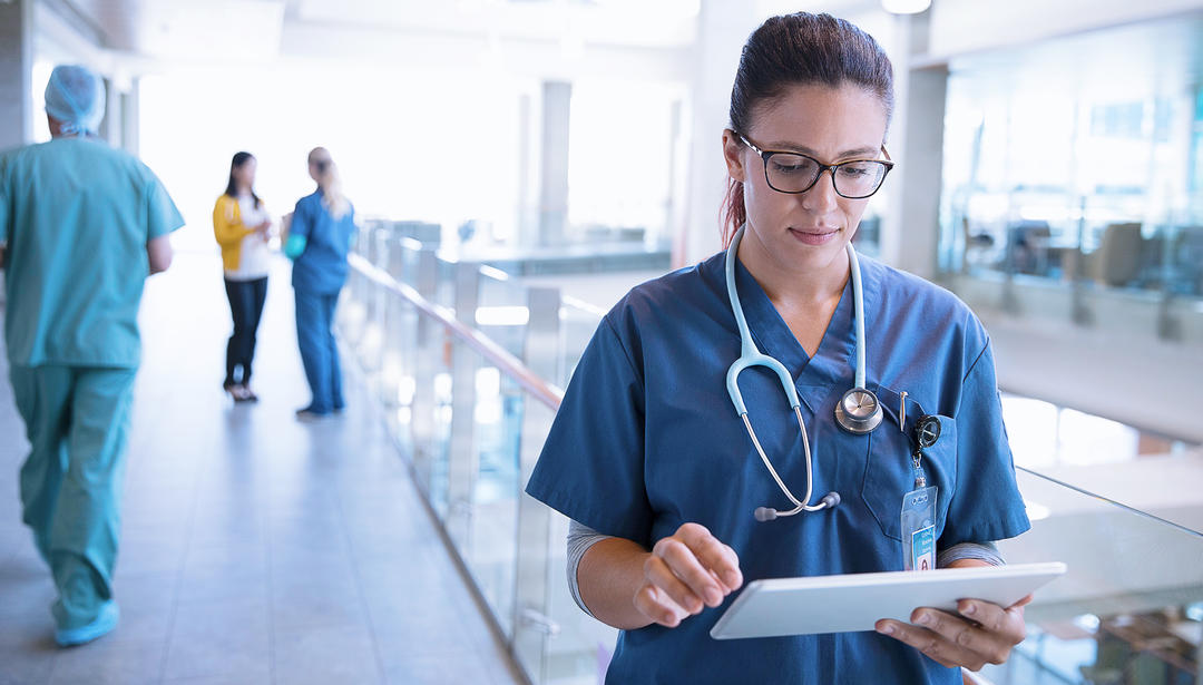 Nurse with stethoscope around her neck walking with tablet