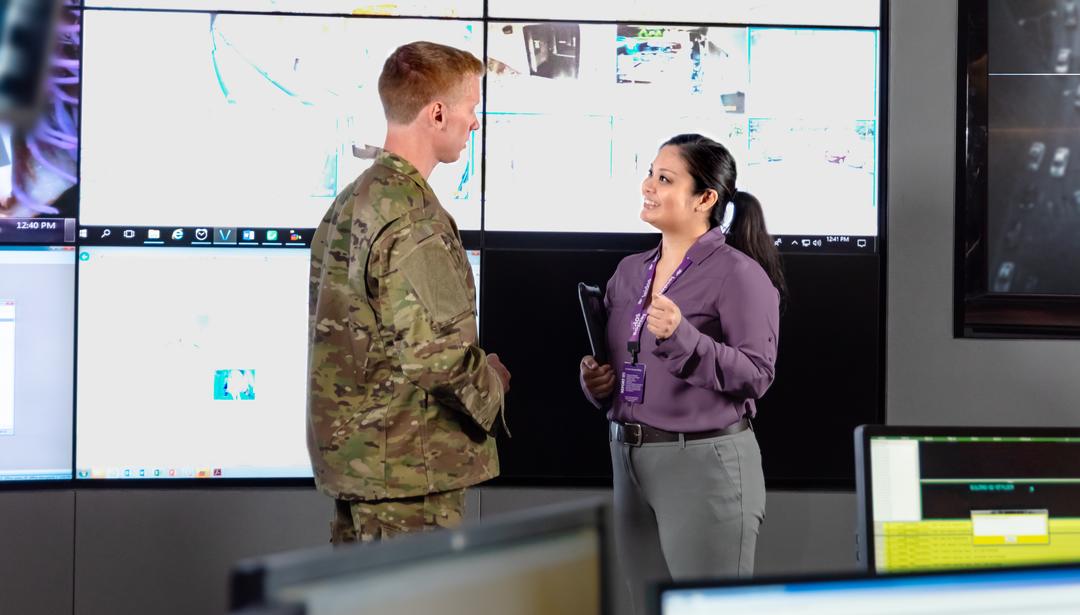 two coworkers talking in-front of screens with data on them