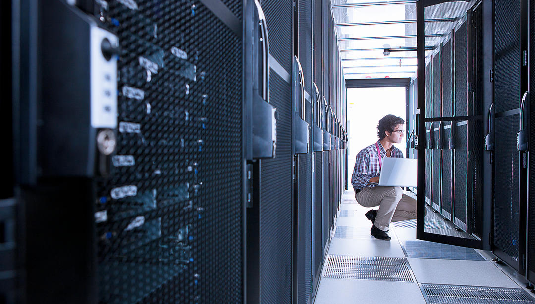 man squatting down with laptop looking inside server cabinet