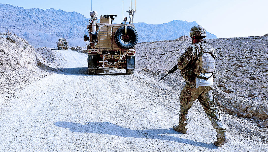 Solider walking behind military vehicle on desert road