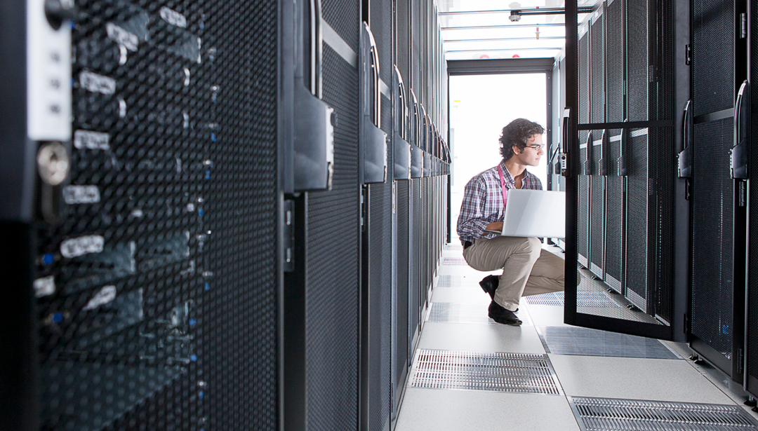 man in server room squatting down with laptop
