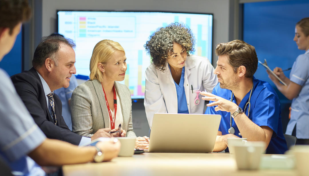 Hospital workers meeting in conference room around laptop