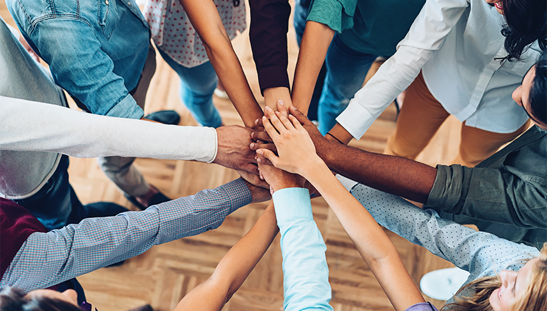 A group of people stood in a circle all with one hand in the middle