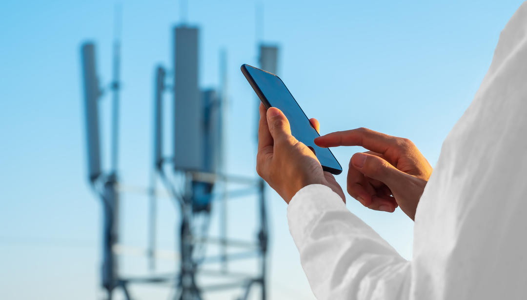 Person using 5G phone with cell tower in background