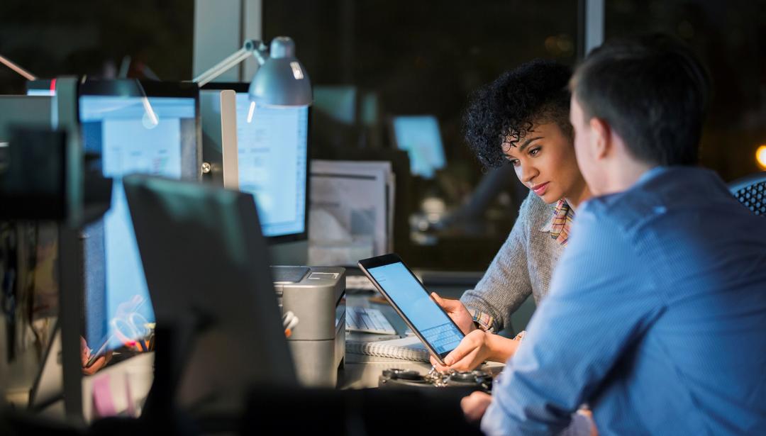 man and woman looking at tablet while sitting in front of workstation