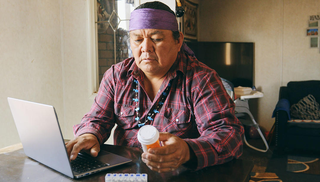 Man holding prescription bottle while using laptop