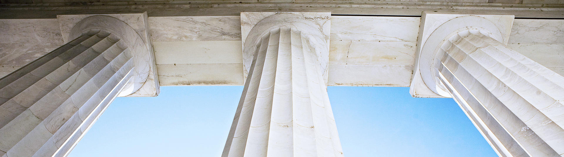 view from the ground looking up at three large marble pillars