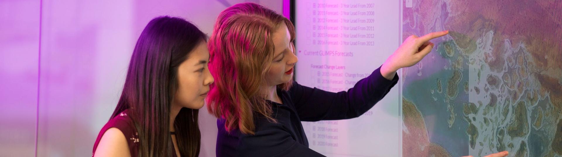 A woman looks on as another points to a map