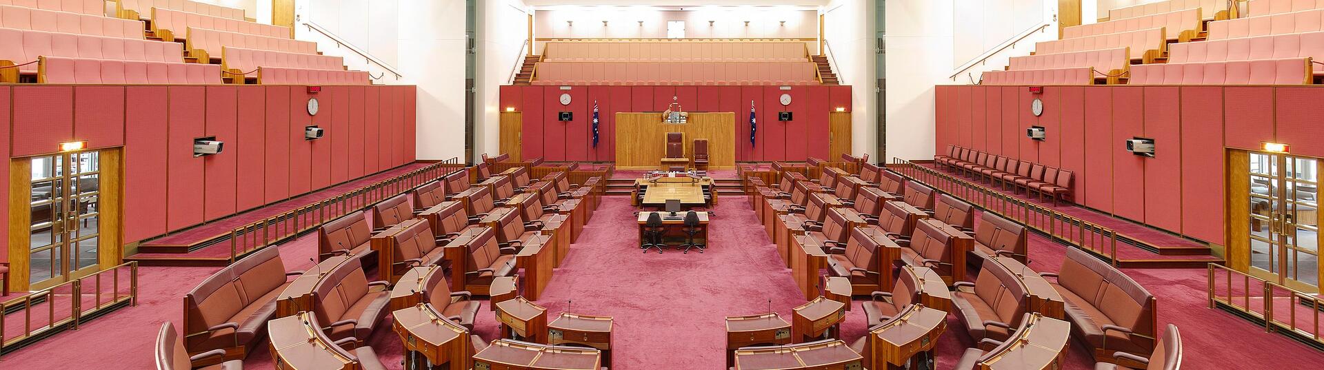 The House of Senate at Australian Parliament House, red seats in a semi circle facing the front of the room.