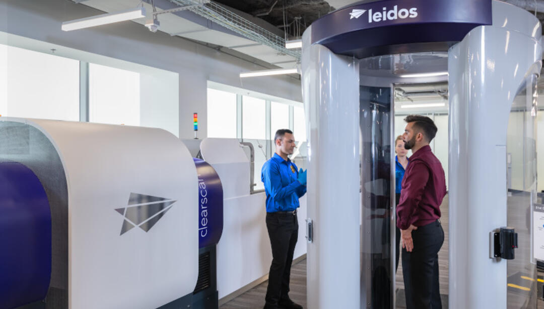 A man in a burgundy shirt standing in a body scanner at the airport. 