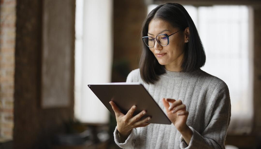 Smiling Asian female entrepreneur working on touchpad in the office.