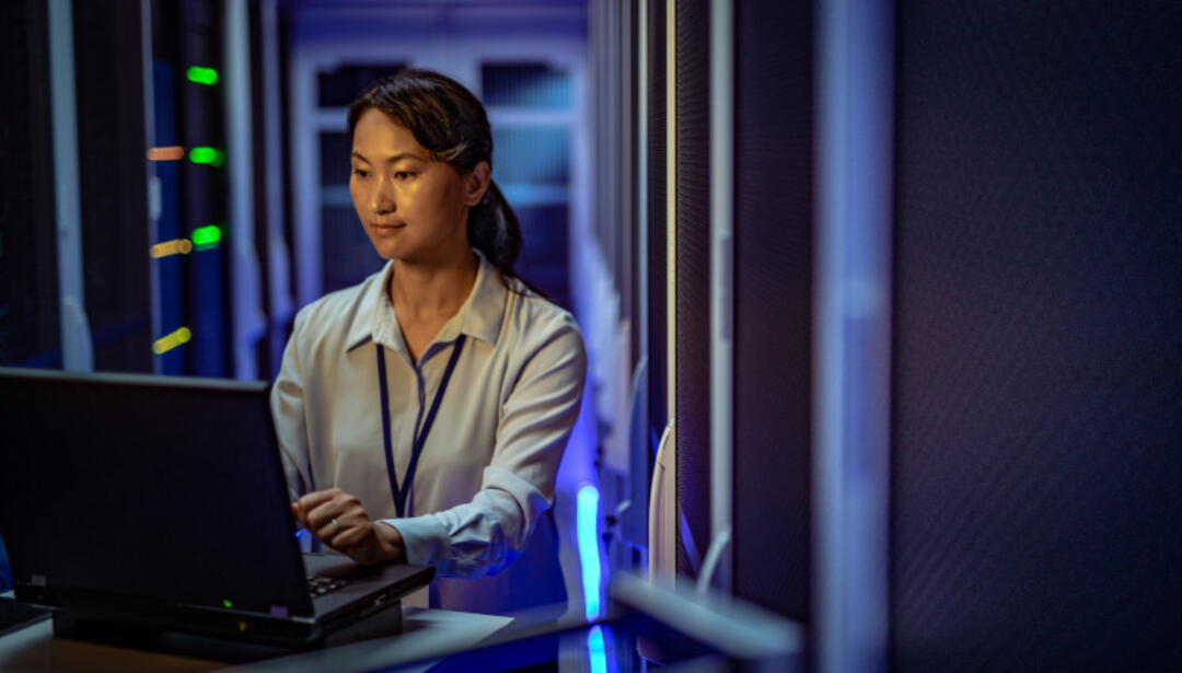 A woman works on a laptop in a data center