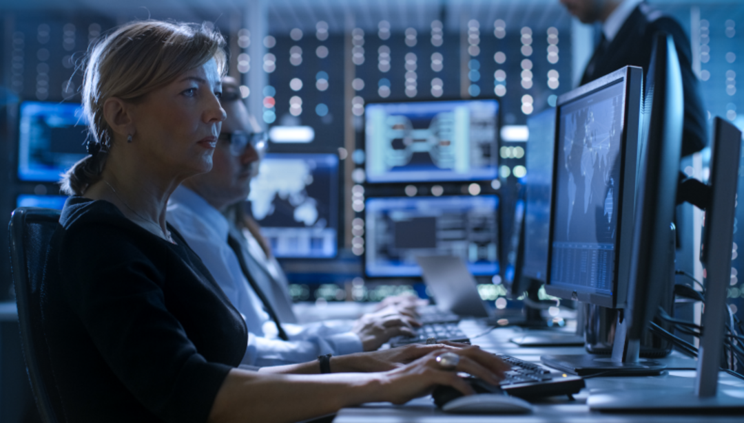 woman and man at desk surrounded by computer monitors