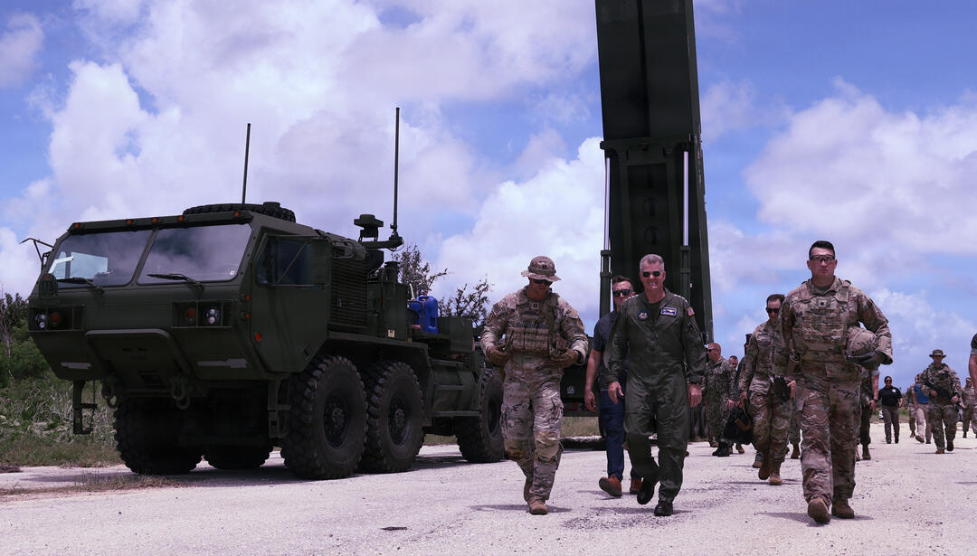 U.S. military personnel and officials walk past a Dark Eagle long-range hypersonic weapon launcher during the Valiant Shield exercise, with the mobile launcher and support vehicle positioned beside the roadway.