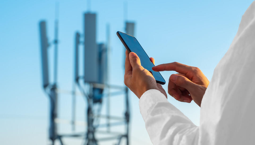 Person using 5G phone with cell tower in background