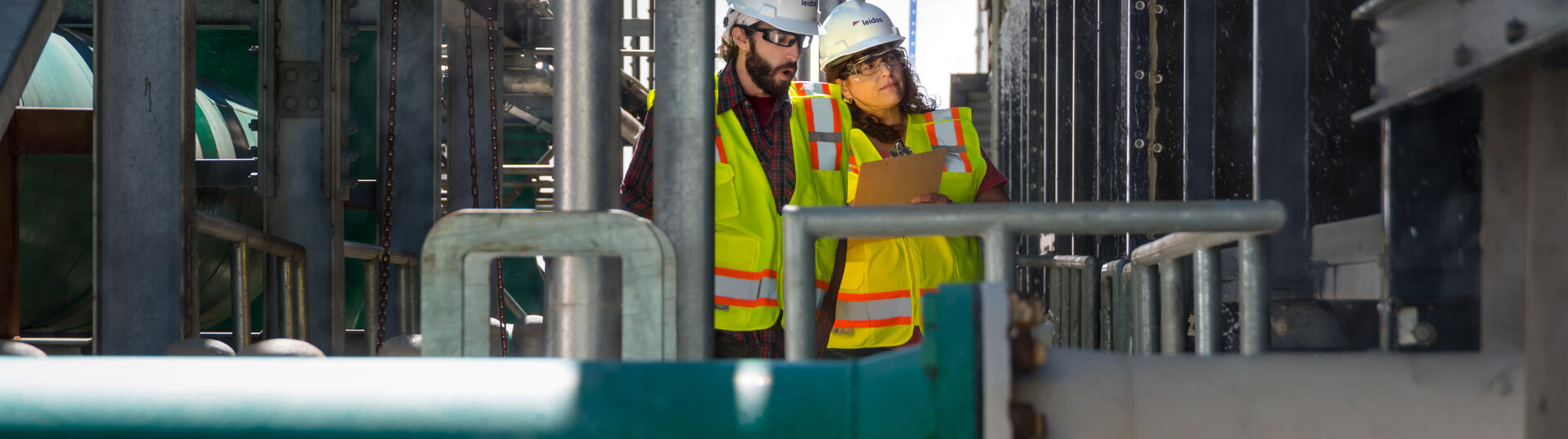 two employees with hardhats reviewing a clipboard
