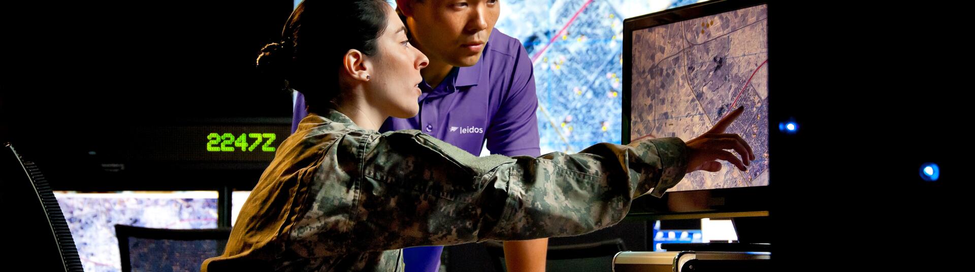 A man looking on as a soldier points at a computer screen