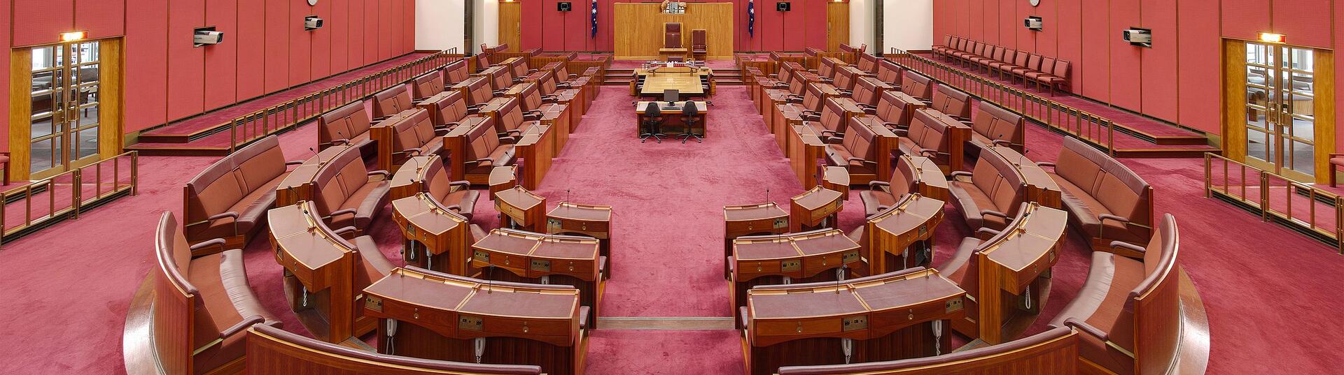 The House of Senate at Australian Parliament House, red seats in a semi circle facing the front of the room.
