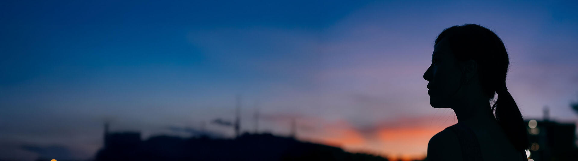 Silhouette of the side profile of young Asian woman looking over sky enjoying twilight in the nature.