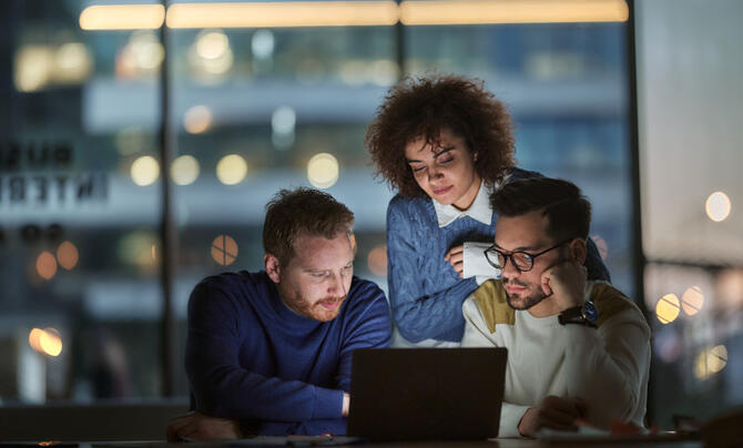 Three technology professionals collaborating around a laptop.