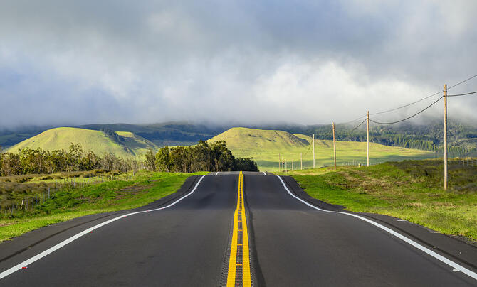 Power line follows a road headed towards rolling hills.