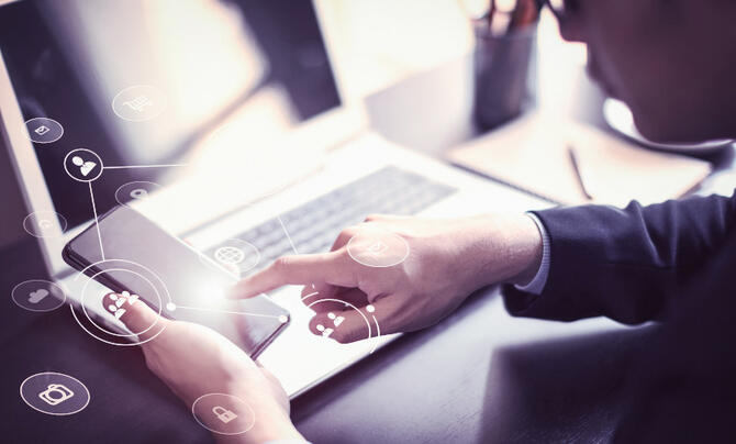 person working on a laptop while looking at their phone