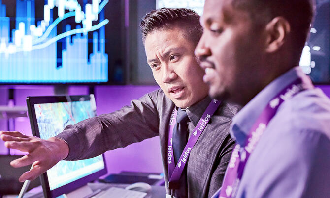 Two professionals review data on computer screens, with one pointing as they discuss.