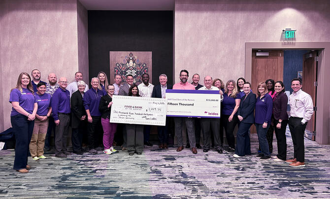 A group of employees stands together indoors holding oversized donation checks for Food Bank of the Rockies during a community fundraising event.