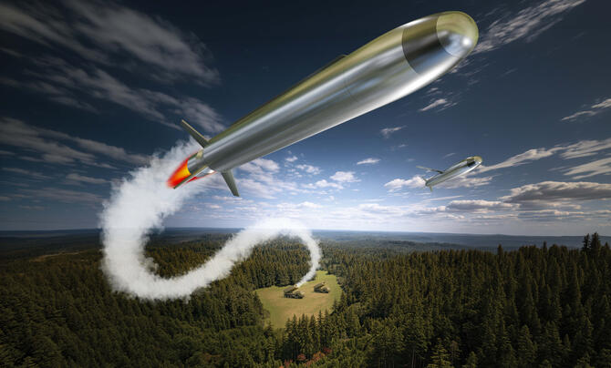A silver missile flying through the sky with a trail of exhaust smoke leading to a launcher in a small clearing in a wooded area.