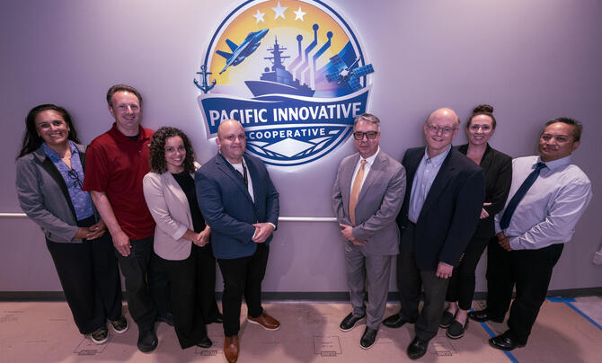 A group of professionals stands together beneath the Pacific Innovative Cooperative logo during a partnership or organizational event.