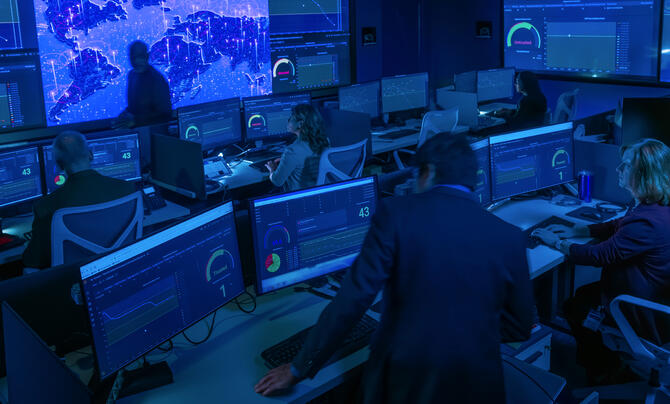 A cybersecurity operations center with analysts monitoring real-time dashboards and global network activity across multiple screens to detect and respond to cyber threats.