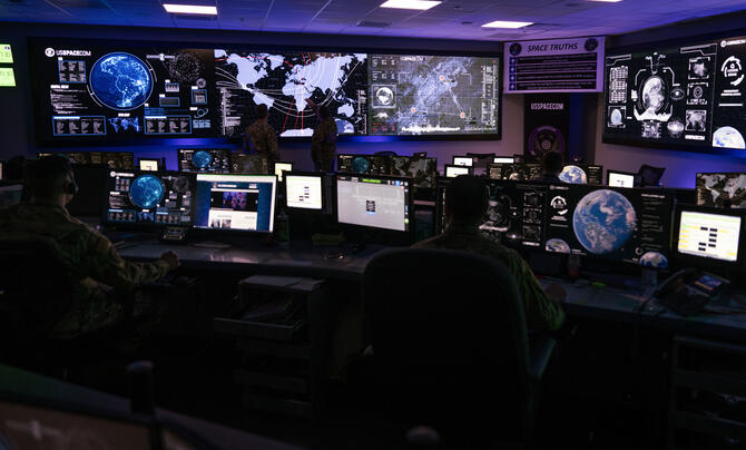 A security operations center with multiple large and small screens showing information, world maps