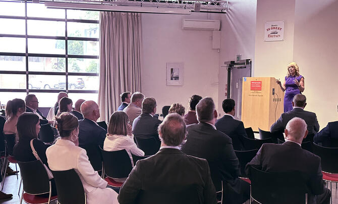 Speaker addresses a seated audience during a professional event in a conference venue.