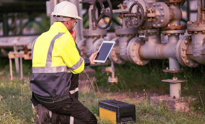Engineer kneeling in front of pipes, holding a tablet.