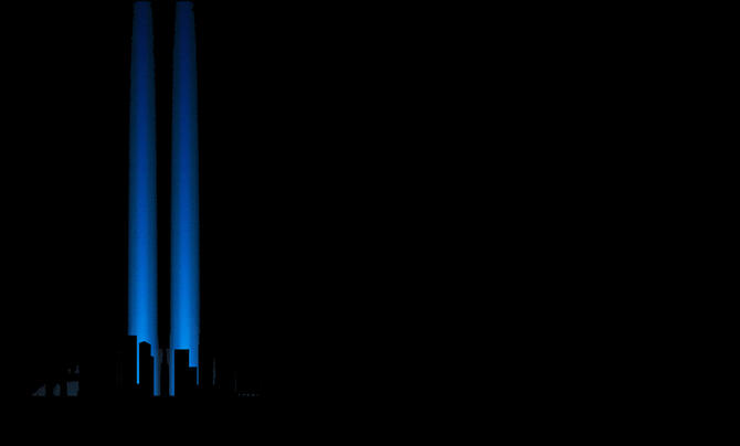 Two blue Tribute in Light beams rise into the night sky above the dark silhouette of Lower Manhattan.