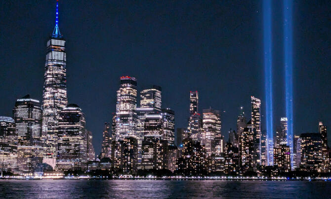 The illuminated New York City skyline at night, with the Tribute in Light beams rising into the sky beside Lower Manhattan.